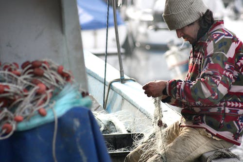 男子坐在蓝色纺织附近坐着渔网 · 免费素材图片