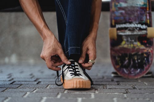 认不出来的人在涂鸦滑板附近的人行道上绑鞋带 · 免费素材图片