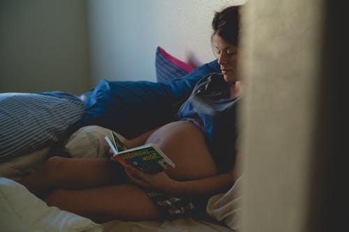 孕妇坐在床上，看书 · 免费素材图片