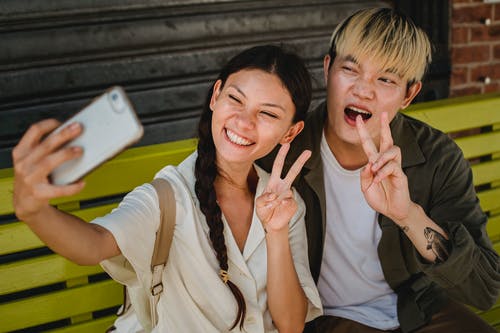 快乐的亚洲夫妻在街头长椅上以智能手机拍照 · 免费素材图片