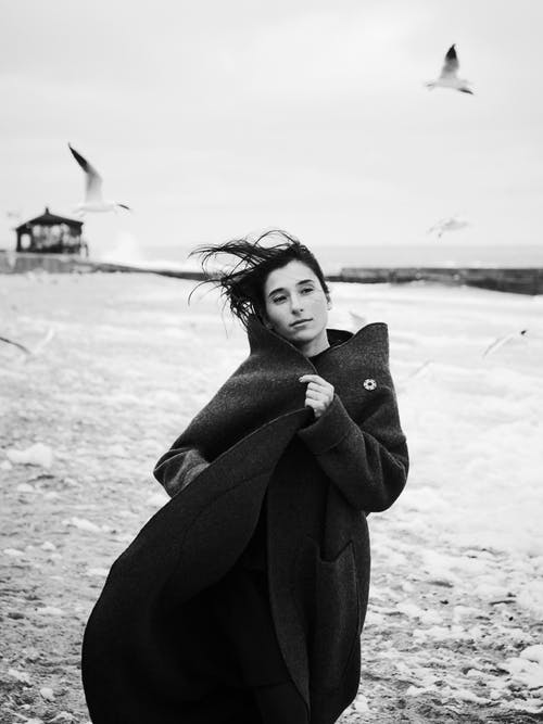穿黑大衣站在海滩上的女人 · 免费素材图片