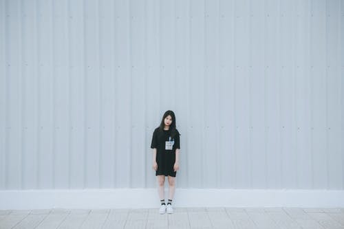 黑色肘袖衬衫和黑色短裤站在白墙后面的女人 · 免费素材图片