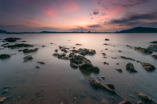 日落期间在水体上的岩石 · 免费素材图片