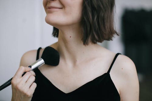 女人穿着黑色意大利面条表带顶部使用化妆刷 · 免费素材图片