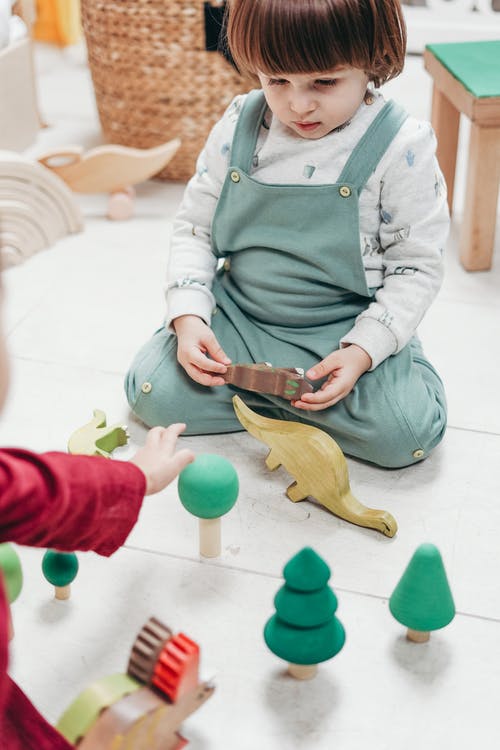 婴儿在绿色围裙，拿着棕色的木制玩具 · 免费素材图片