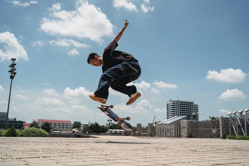 族裔男子在人行道上与滑板跳 · 免费素材图片