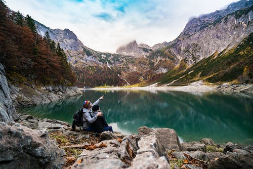 夫妻坐在湖边的岩石上 · 免费素材图片
