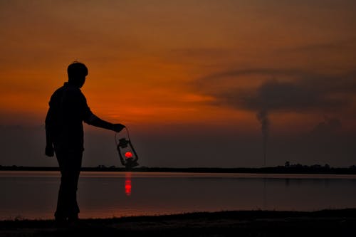 人与油灯在日落时在岸上的剪影 · 免费素材图片