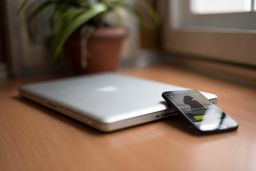 智能手机旁边棕色背景与盆栽植物的木桌上的银色macbook · 免费素材图片