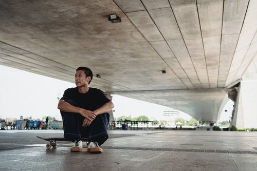 有休息在具体建筑下的滑板的体贴的亚裔年轻人 · 免费素材图片