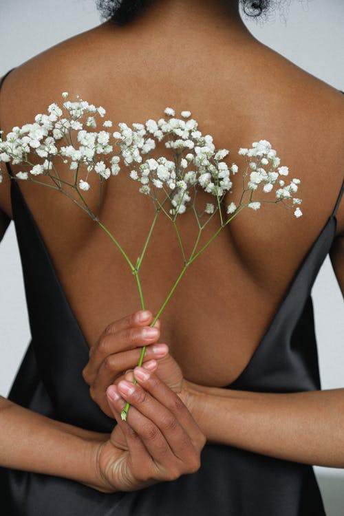在黑色的晚礼服，在她的背后捧着白花的女人的特写照片 · 免费素材图片