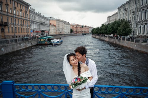 夫妇站在河与蓝色和白色的小船在河上桥 · 免费素材图片