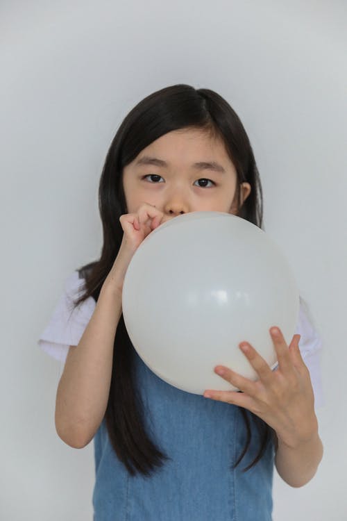 可爱的族裔孩子在工作室里膨胀白色气球 · 免费素材图片