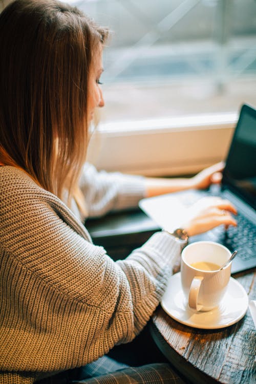 使用便携式计算机的棕色毛衣的女人 · 免费素材图片