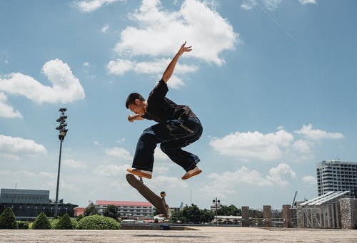 亚洲男子在滑板上执行kickflip · 免费素材图片