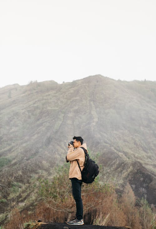 男子背着背包跨山的照片 · 免费素材图片