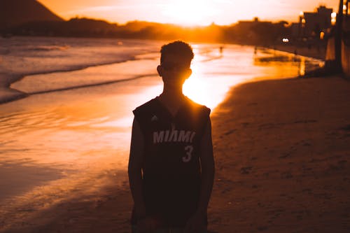 黑色背心，日落期间站在海滩上的人 · 免费素材图片