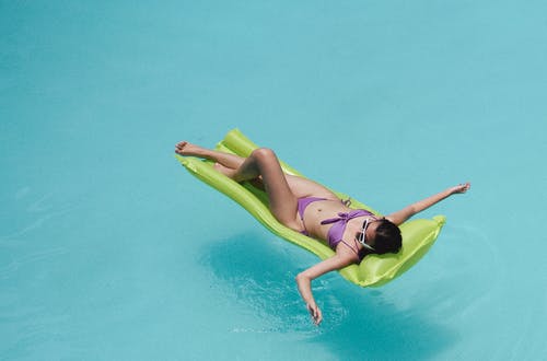 泳装在游泳池充气床垫上晒日光浴的女性 · 免费素材图片