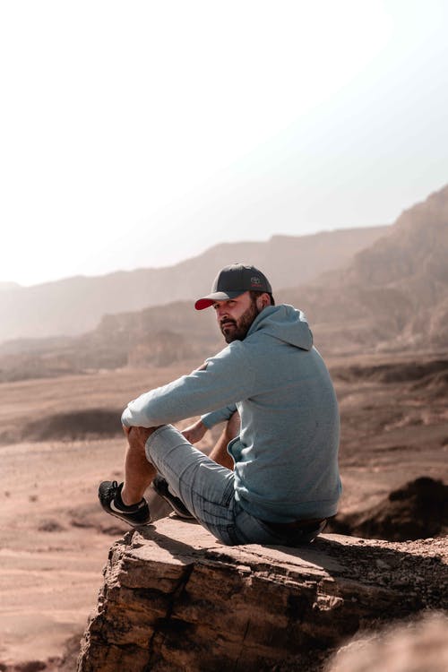 灰色连帽衫和灰色裤子坐在棕色岩石上的男人 · 免费素材图片