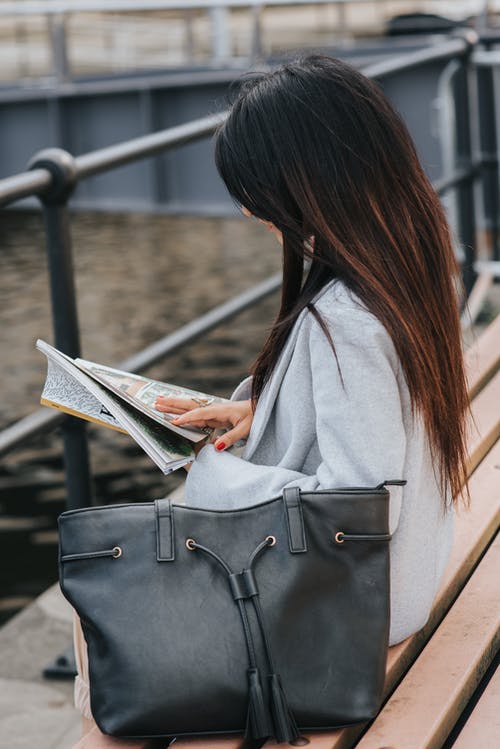 女人在城市海滨的长椅上读书杂志 · 免费素材图片