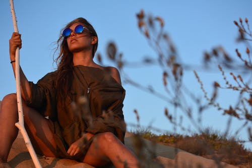 坐在绿色的植物，在湛蓝的天空下附近的棕色衬衫的女人 · 免费素材图片