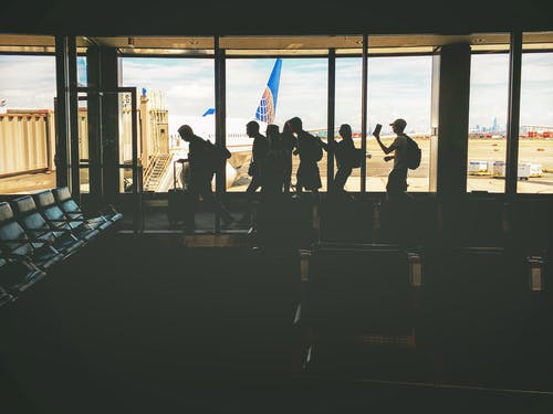 一群人走在透明的玻璃窗附近，白天停着白色飞机 · 免费素材图片