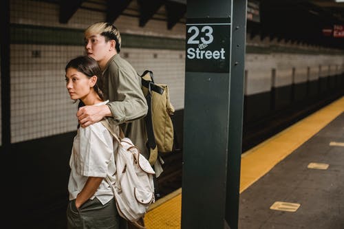 穿着棕色大衣的人站在黑金属后亚洲夫妇在地铁站里等待一列火车 · 免费素材图片