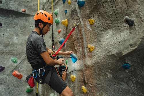 亚洲技术员在安全绳上挂着的同时用螺丝刀在攀岩举行洞 · 免费素材图片
