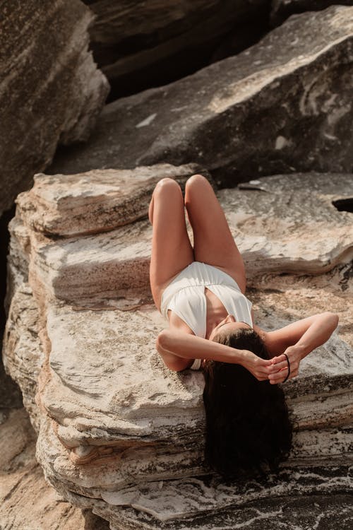躺在岩石上，举起手来的女人 · 免费素材图片