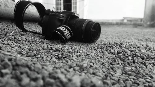 尼康dslr相机与瓦砾灰度照片放在地面上 · 免费素材图片