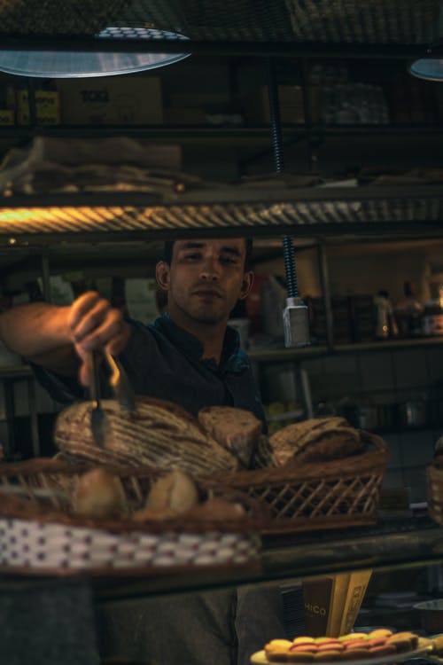 蓝色按钮衬衫用面包钳捡面包的人 · 免费素材图片