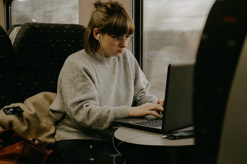 使用便携式计算机的灰色毛衣的女人 · 免费素材图片