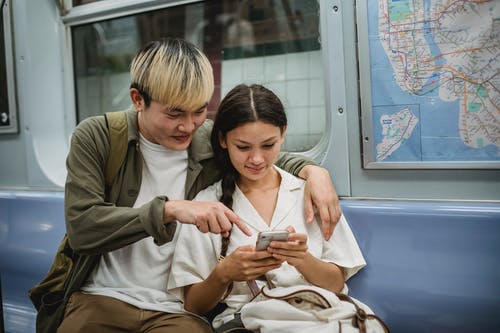 积极年轻的种族夫妇拥抱和在火车上使用智能手机 · 免费素材图片