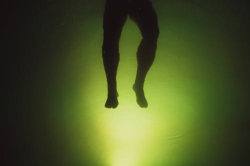 匿名男子在绿色背景附近的水中游泳 · 免费素材图片