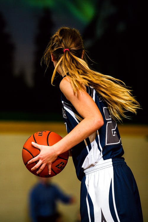 拿着棕色篮球的蓝色和白色篮球球衣的女人 · 免费素材图片