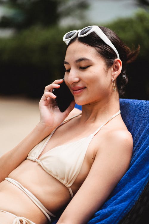 谈到智能手机和在躺椅上晒日光浴的快乐年轻种族女人 · 免费素材图片