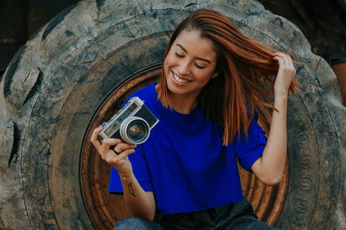 女人穿着蓝色t恤，拿着相机的浅焦点照片 · 免费素材图片