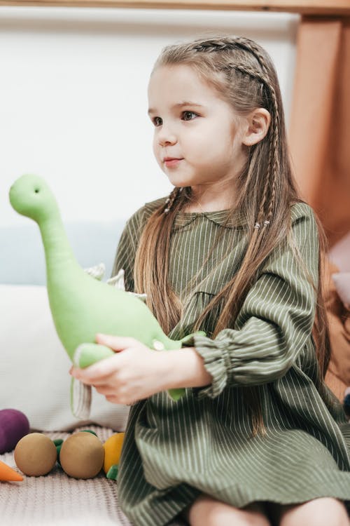 拿着毛绒玩具时穿绿色的裙子的女孩 · 免费素材图片