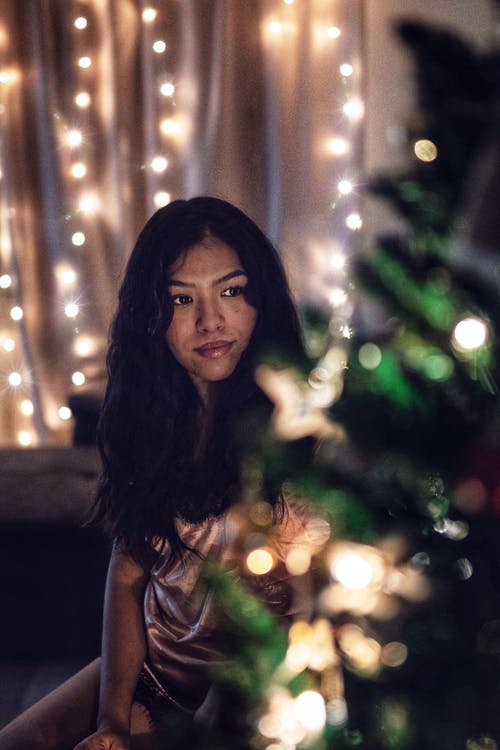 女人站在圣诞树旁边的灯串 · 免费素材图片