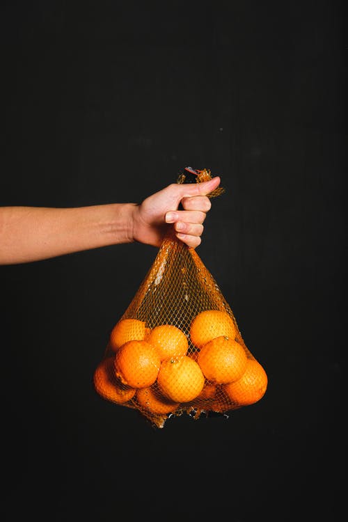 拿着橙色网和束橙色水果的人 · 免费素材图片