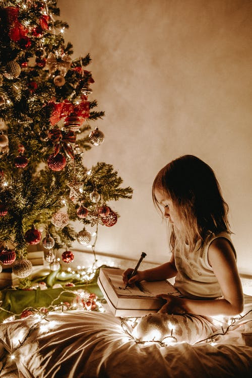 坐在圣诞树旁的女孩的照片 · 免费素材图片