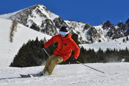 一个男人穿着橙色外套和米色长裤滑雪的照片 · 免费素材图片
