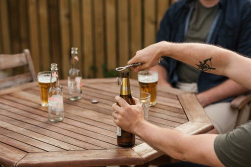 男子与朋友在木桌上休息时打开啤酒 · 免费素材图片