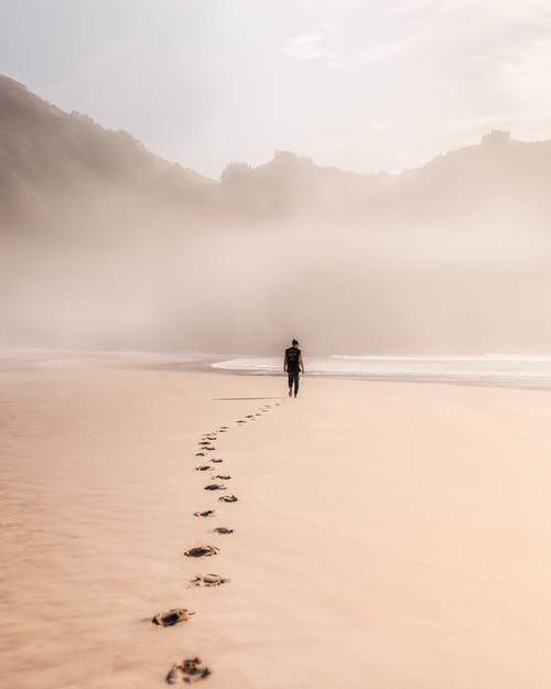 在有雾的天气中在沙质海滨上行走的匿名男子 · 免费素材图片