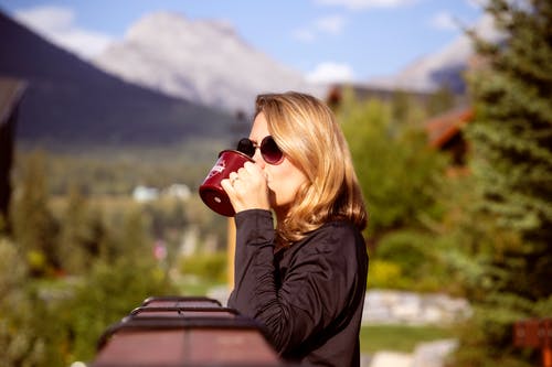 黑色长袖衬衫在栗色陶瓷杯上喝酒的女人的浅焦点照片 · 免费素材图片