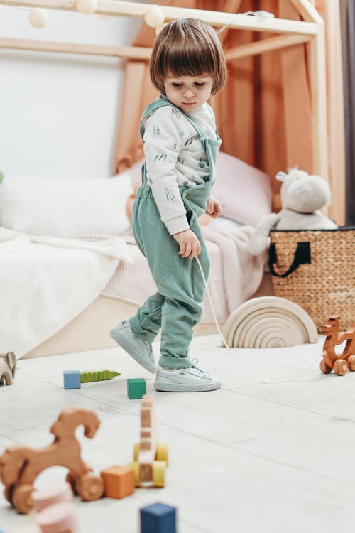 白色长袖上衣和绿色粗斜纹棉布长裤的孩子玩的玩具 · 免费素材图片