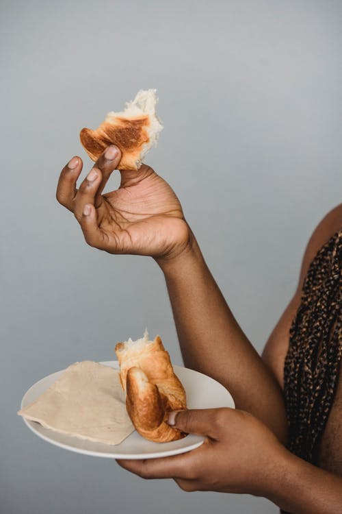 作物无法辨认的黑人男子，吃新鲜的牛角包 · 免费素材图片