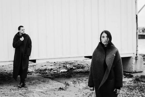 女人和男人穿着黑大衣，站在白墙附近 · 免费素材图片