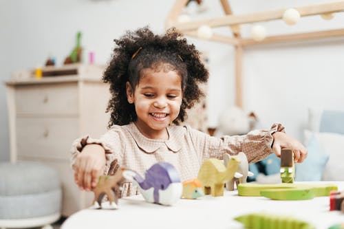 选择聚焦照片的微笑的年轻女孩，在白色的桌子上玩木制玩具 · 免费素材图片