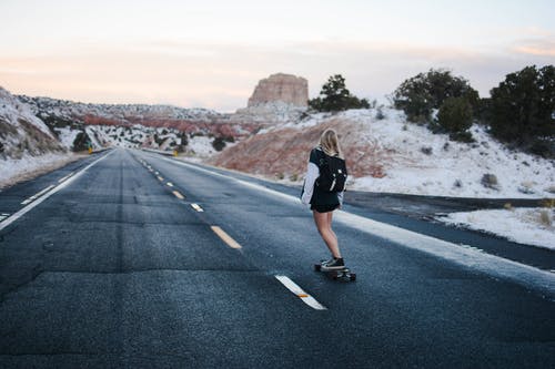 黑色和白色的长袖衬衫，在高速公路上骑滑板的女人 · 免费素材图片